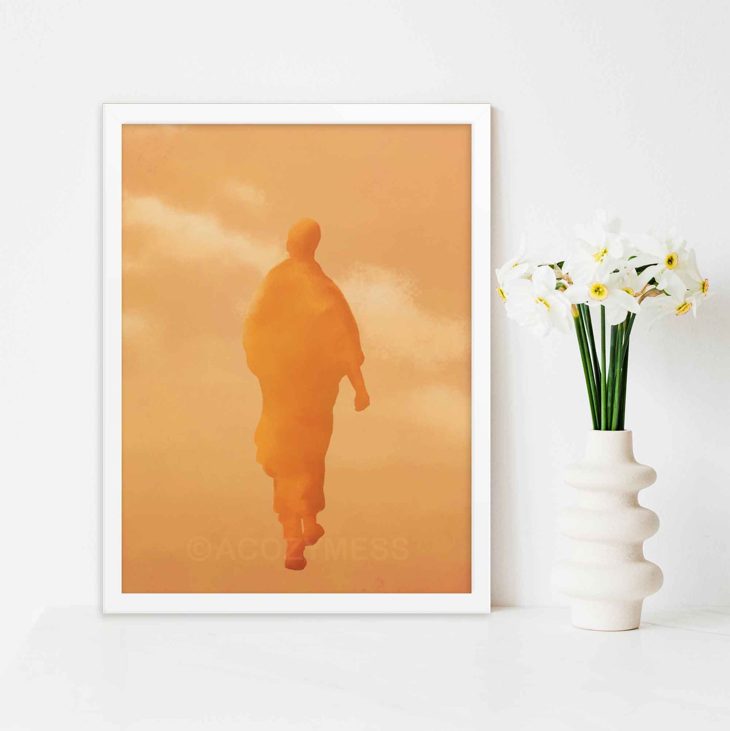 Art print of a walking monk in warm orange and yellow hues, capturing serenity and spiritual presence, in white frame.