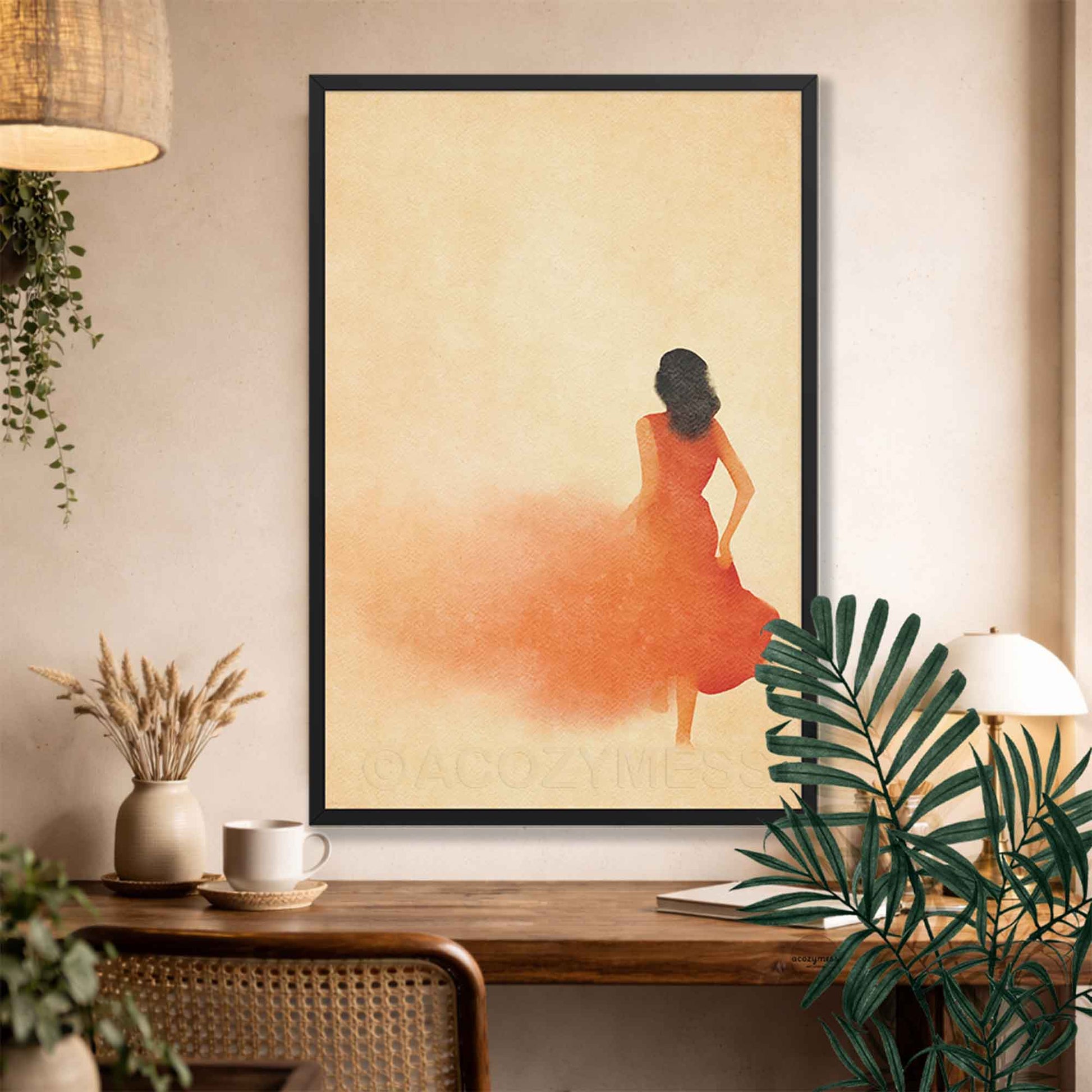 Black Framed artwork of a woman in an orange dress on a wall above a wooden desk with plants.