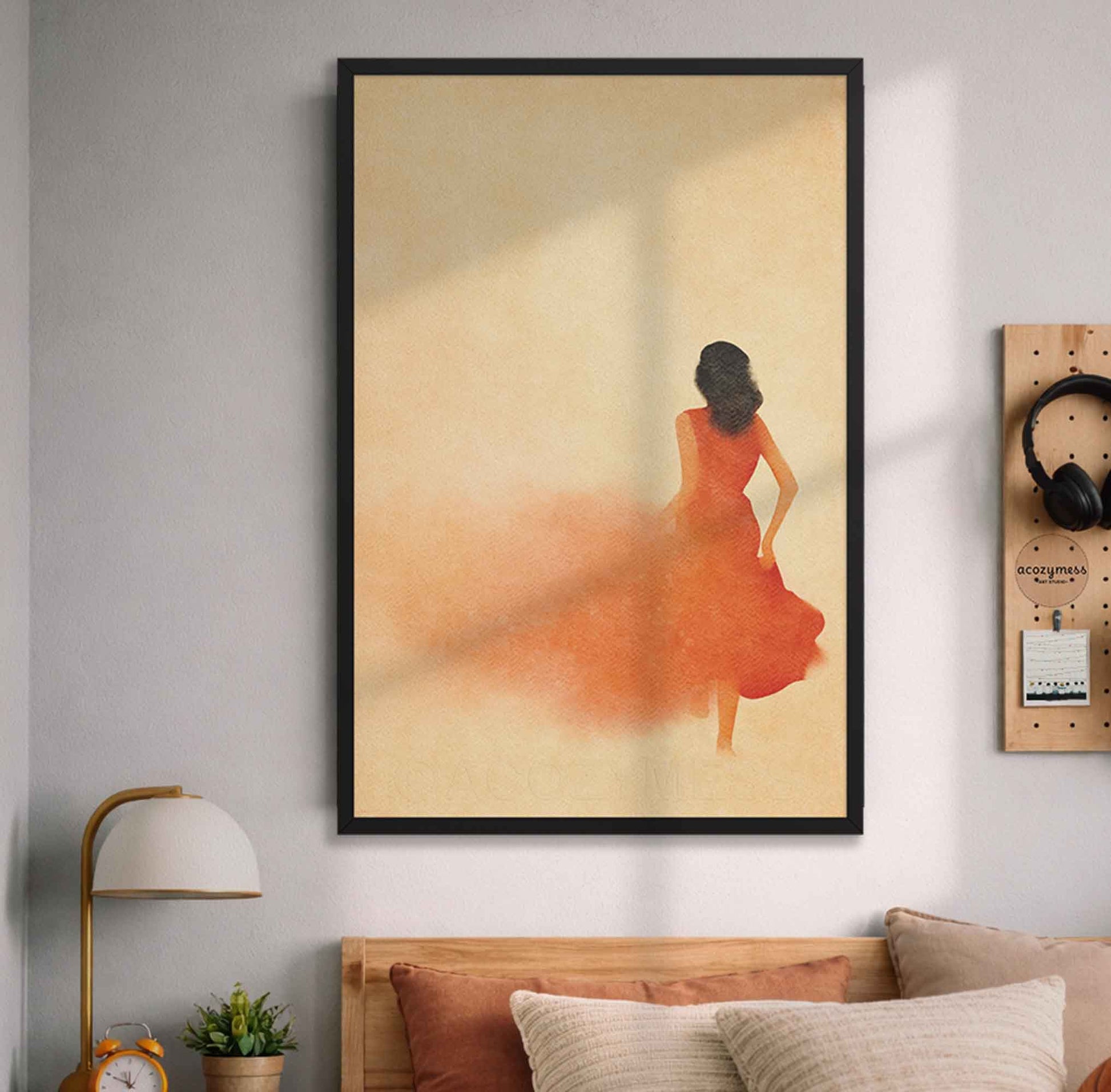 Framed artwork of a woman in an orange dress on a wall above a bed.