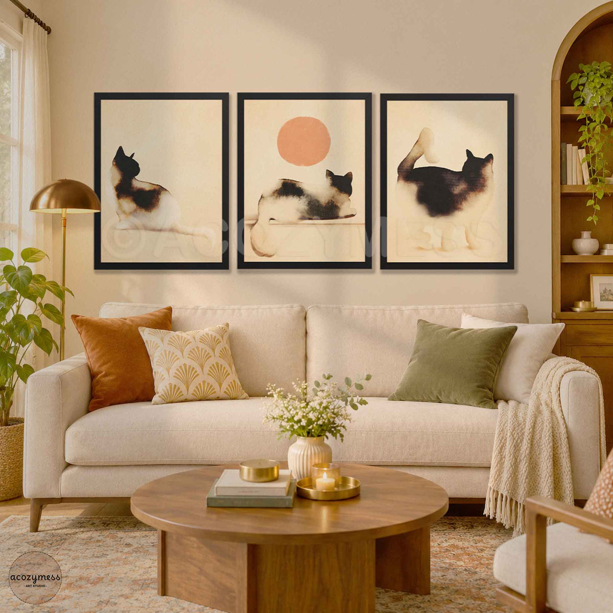 Three black framed minimalist watercolor cat prints with the cat and peach sun poster in the center above a cream sofa in a warm living room