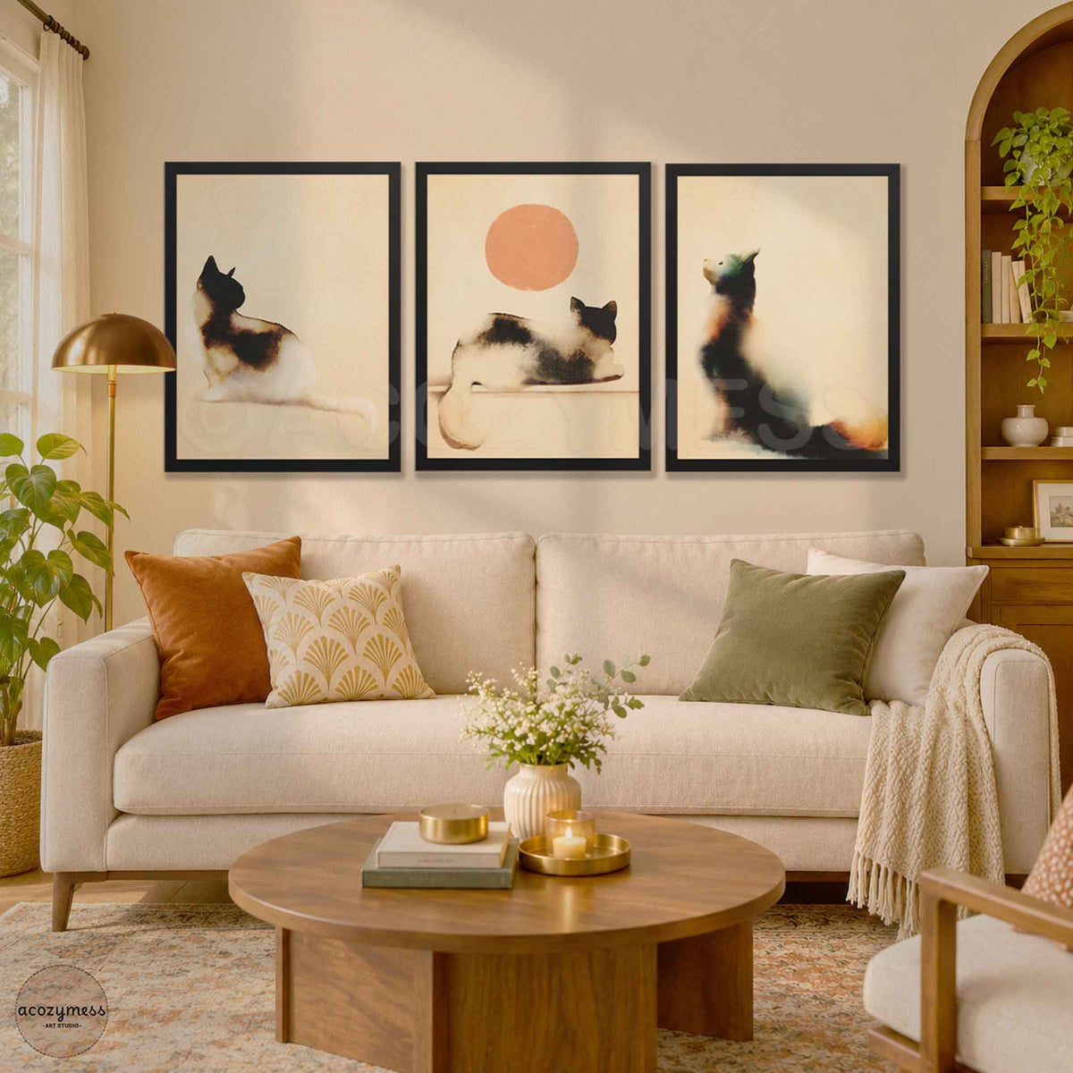 Gallery wall of three black framed watercolor cat posters including the cat looking at the sun print above a cream sofa