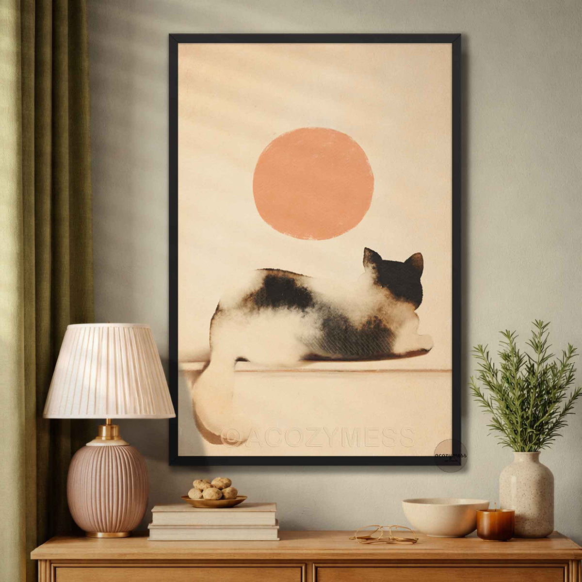 Black framed minimalist cat and sun art print above a wooden sideboard with a pink lamp and potted plant