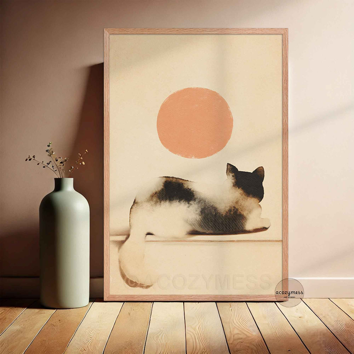 Light oak framed watercolor cat and peach sun poster leaning against a blush wall beside a sage green vase