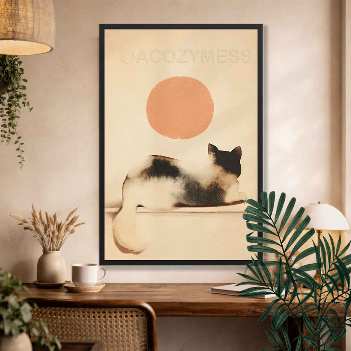 Black framed cat and sun wall art above a wooden desk with dried flowers and a palm plant
