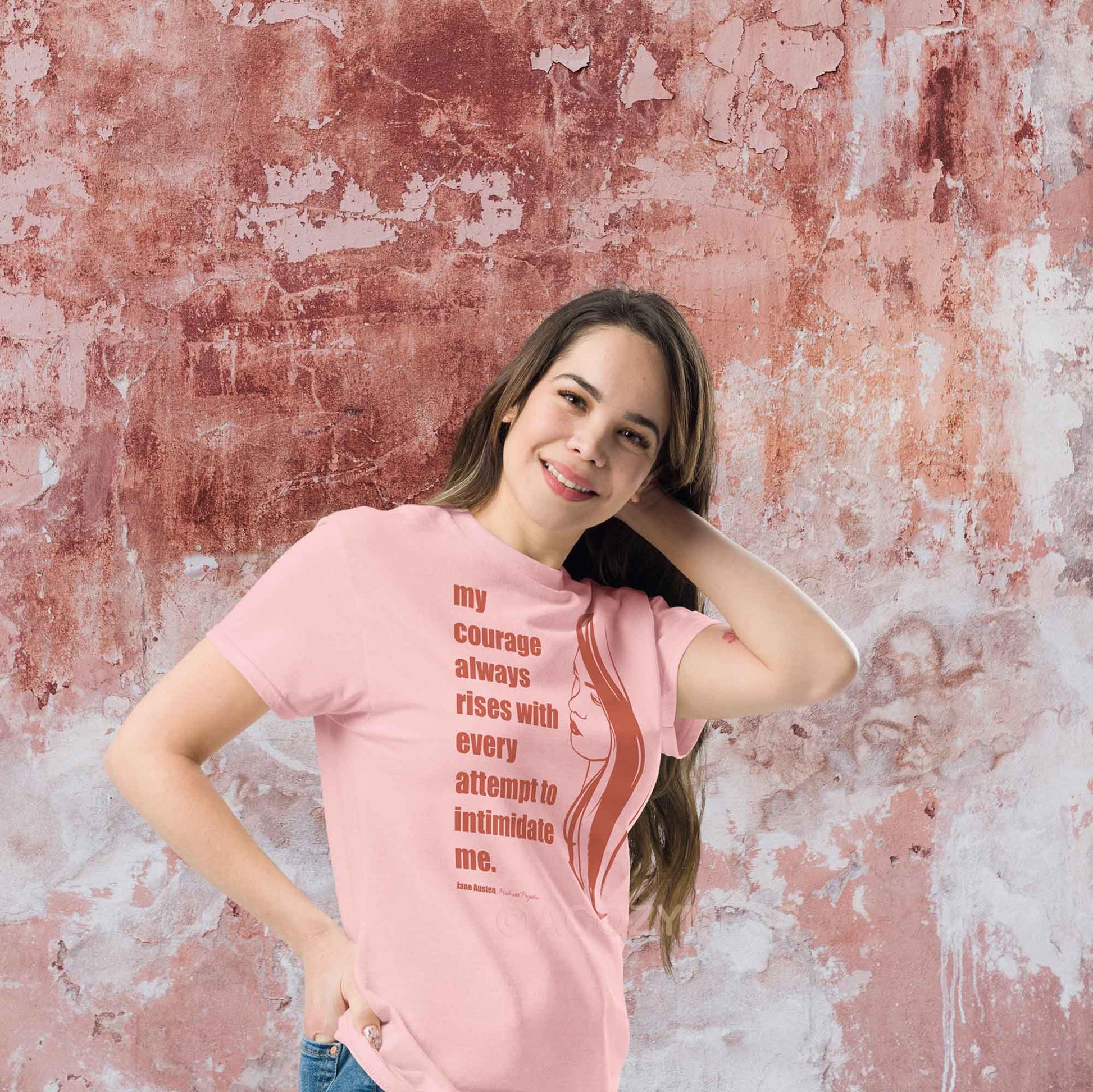 A woman wearing pink T-shirt featuring a  illustration of a woman portrait alongside a Jane Austen quote: "Courage always rises with every attempt to intimidate me.