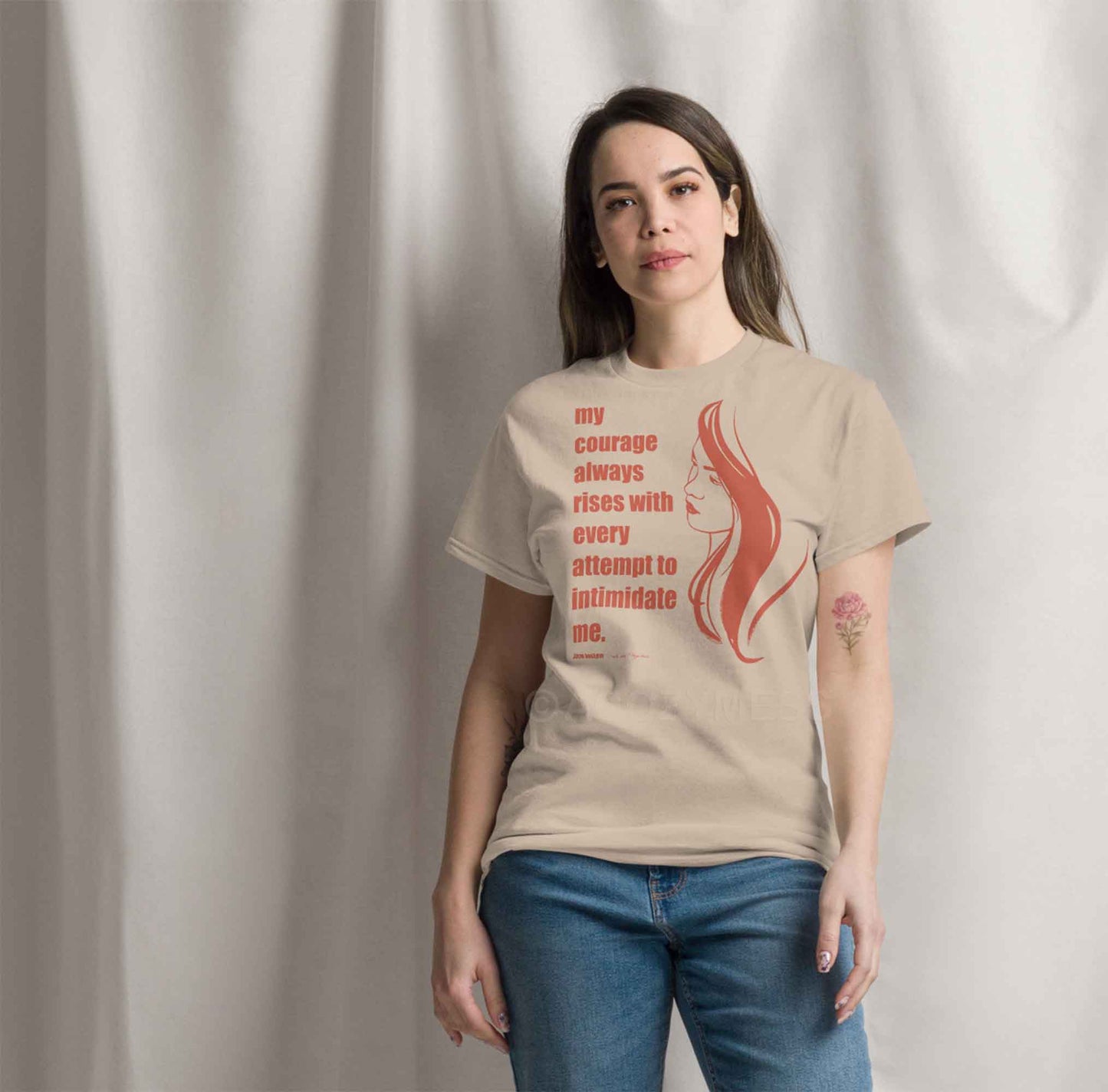 A woman wearing sand color T-shirt featuring a  illustration of a woman portrait alongside a Jane Austen quote: "Courage always rises with every attempt to intimidate me.