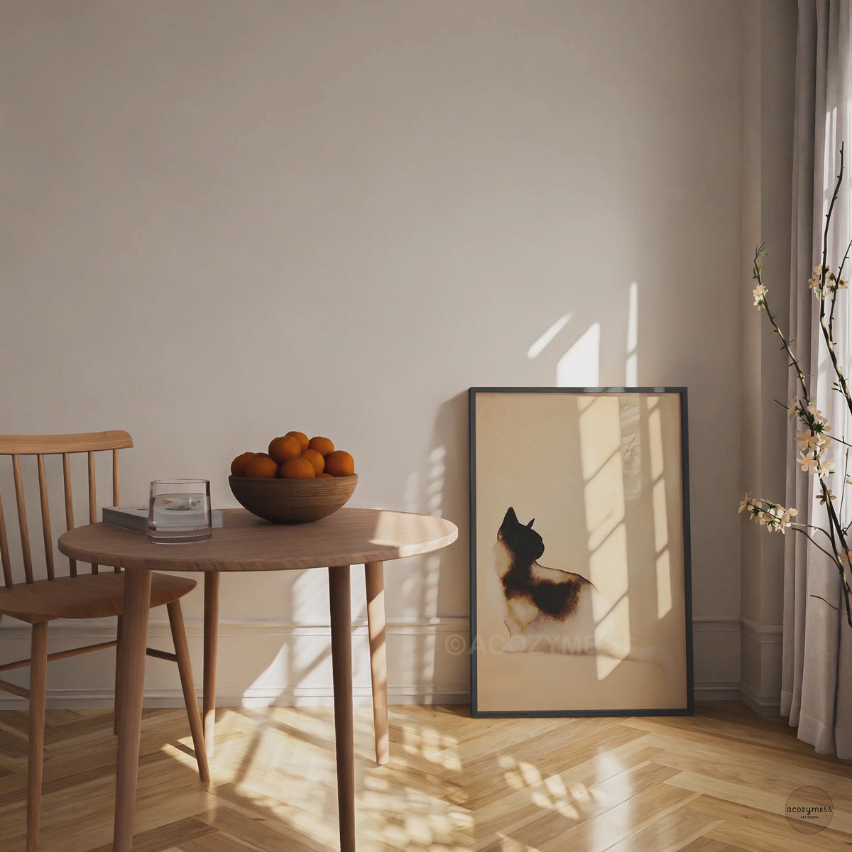 Video of a black framed minimalist watercolor cat art poster leaning on the floor beside a wooden dining table in warm sunlight
