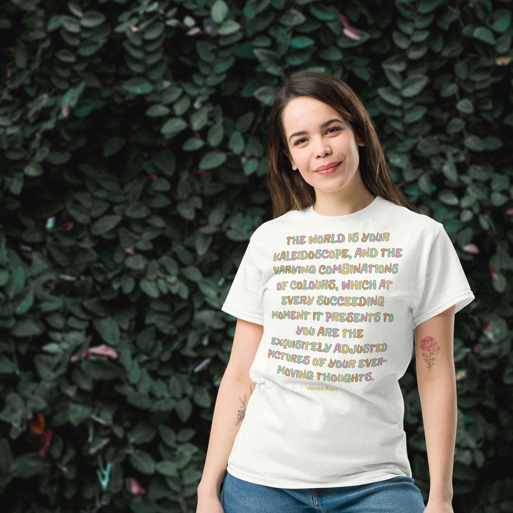 A woman wearing white typography T-shirt featuring an inspiring quote by James Allen: The world is your kaleidoscope, and the varying combinations of colors, which at every succeeding moment it presents to you are the exquisitely adjusted pictures of your ever-moving thoughts.