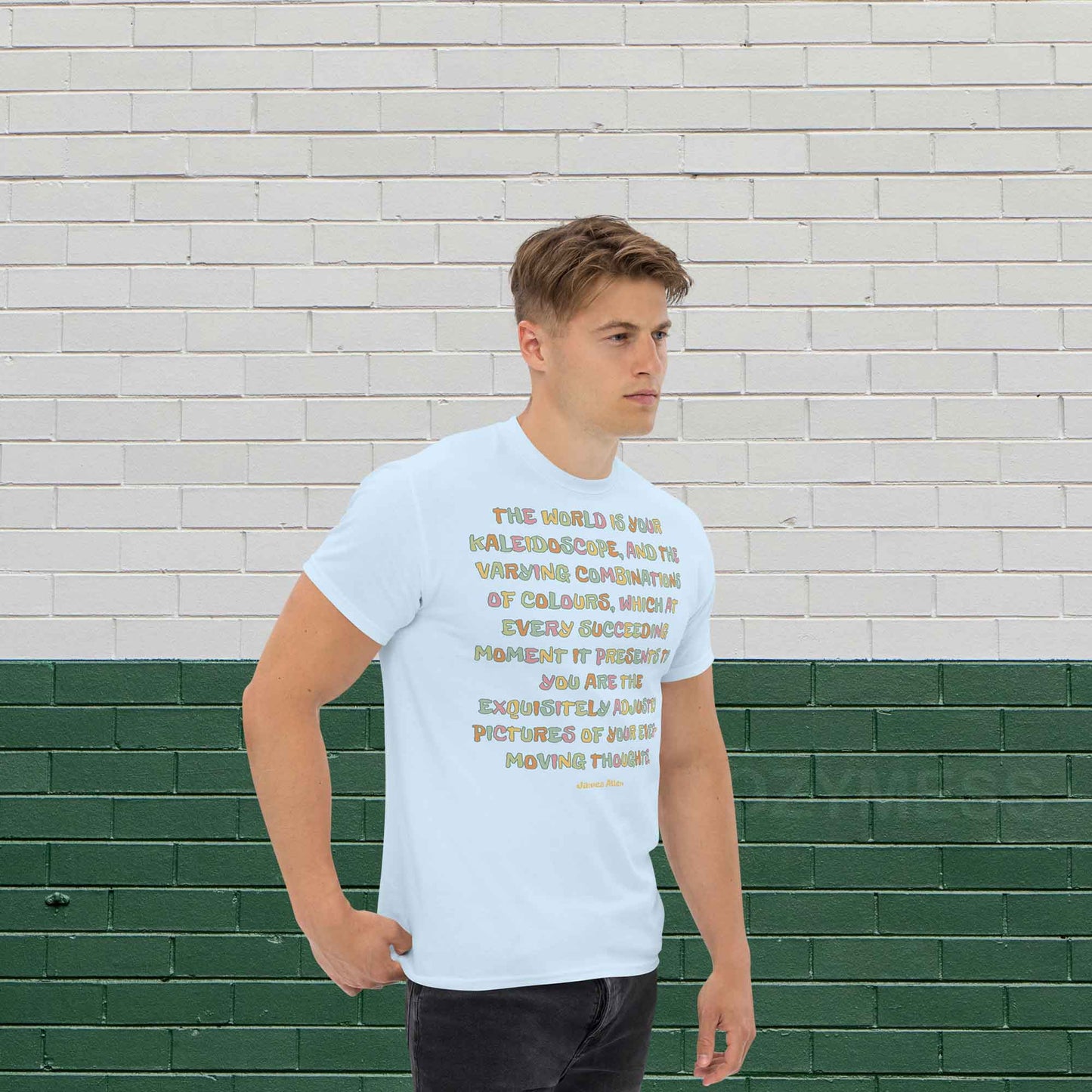 A man wearing light blue typography T-shirt featuring an inspiring quote by James Allen: The world is your kaleidoscope, and the varying combinations of colors, which at every succeeding moment it presents to you are the exquisitely adjusted pictures of your ever-moving thoughts.