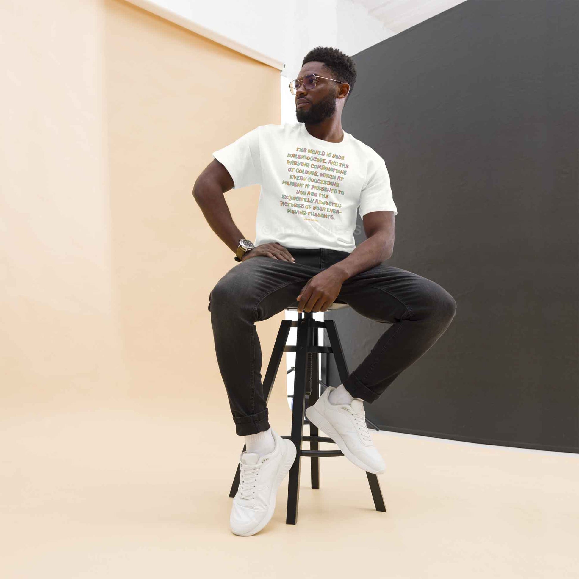 A man wearing white typography T-shirt featuring an inspiring quote by James Allen: The world is your kaleidoscope, and the varying combinations of colors, which at every succeeding moment it presents to you are the exquisitely adjusted pictures of your ever-moving thoughts.