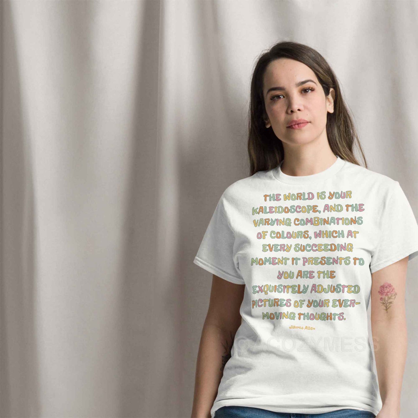 A woman wearing white T-shirt featuring an inspiring quote by James Allen: The world is your kaleidoscope, and the varying combinations of colors, which at every succeeding moment it presents to you are the exquisitely adjusted pictures of your ever-moving thoughts.