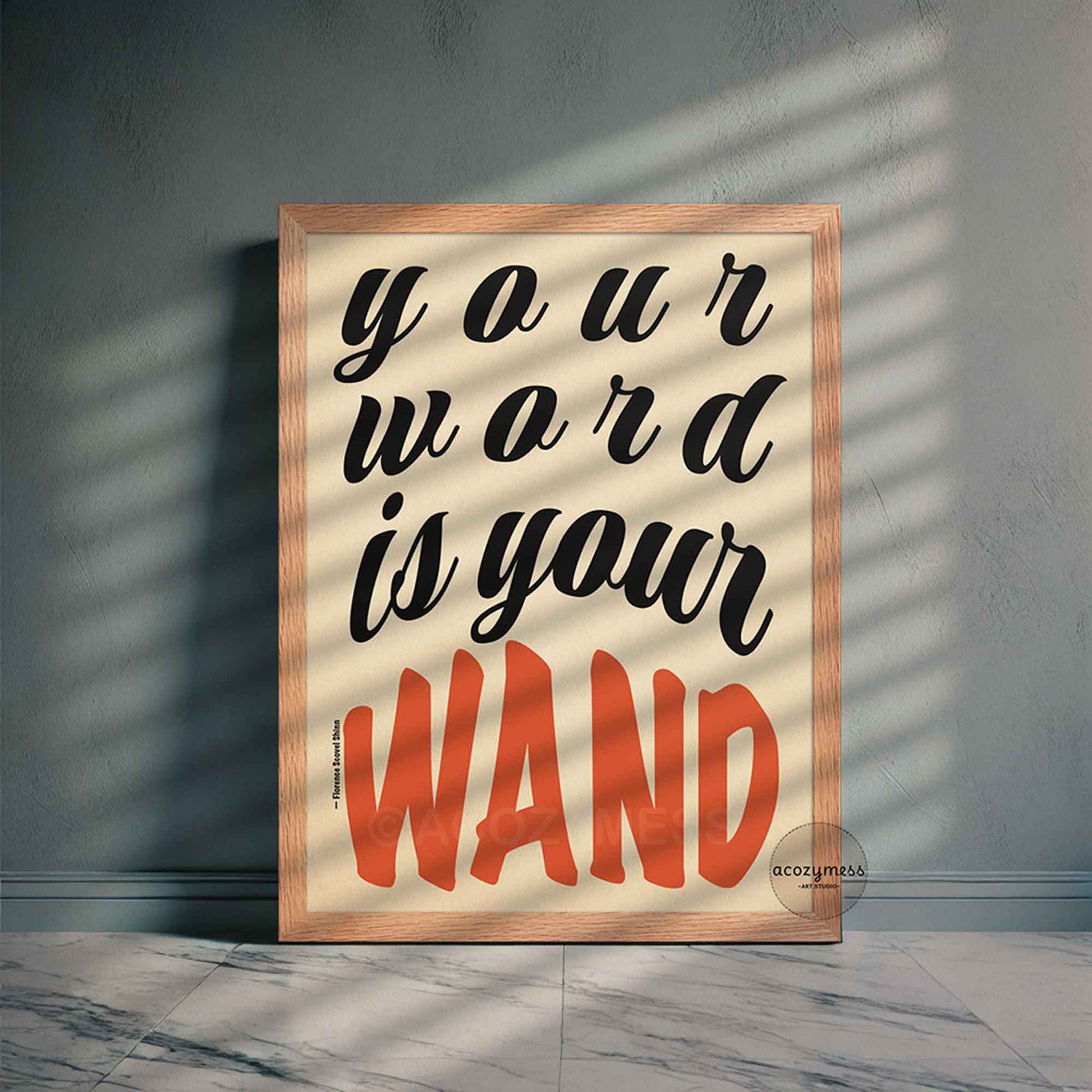 Framed poster of Florence Shinn’s quote “Your Word Is Your Wand” in black and red typography on beige, displayed in an oakwood frame on a neutral-toned wall.